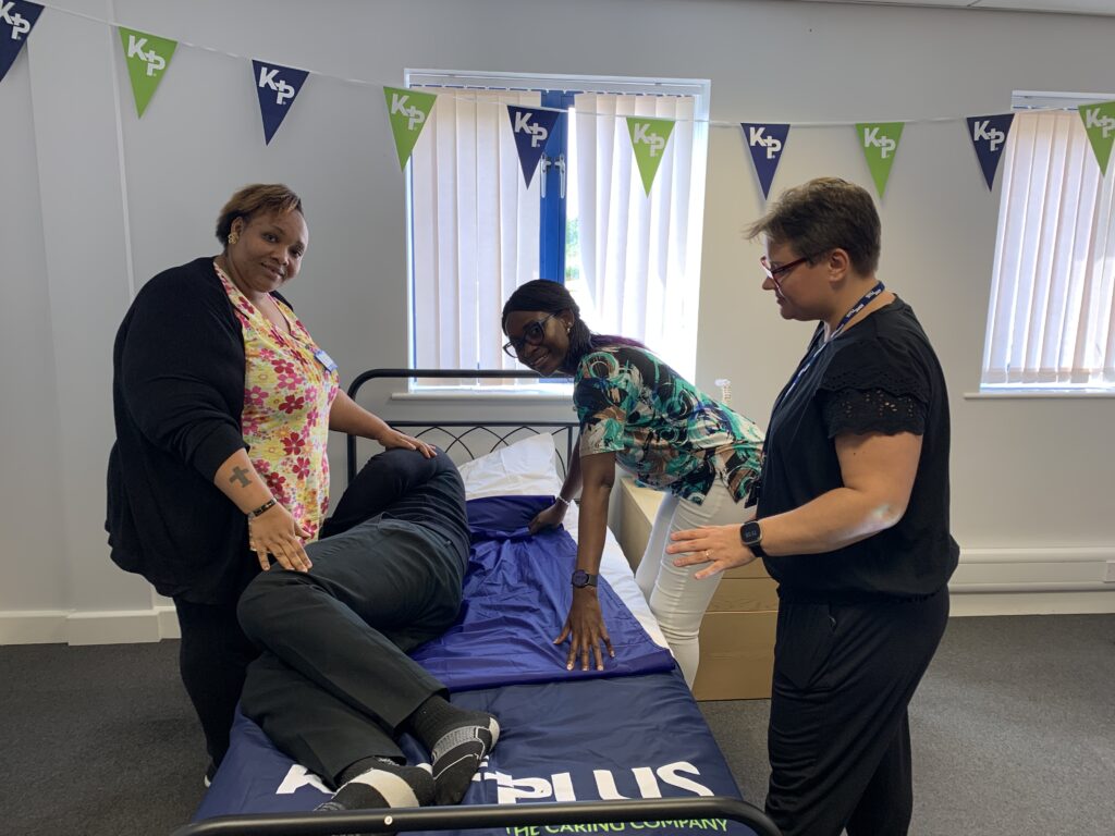 Two female carers practice moving a patient on the bed using an undersheet.